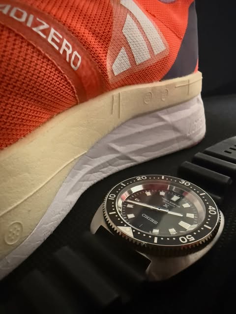 Orange Adidas Adizero running shoe beside a Seiko diver’s watch