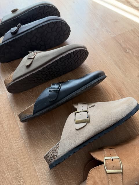 Suede and leather buckle clogs lined up on a wood floor