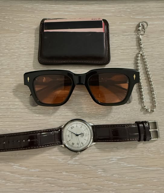 Brown card case, black sunglasses, and a dress watch with Roman numerals